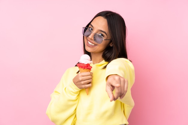 Jong donkerbruin meisje dat een cornetroomijs over geïsoleerd roze houdt die telefoongebaar maakt en voorzijde richt