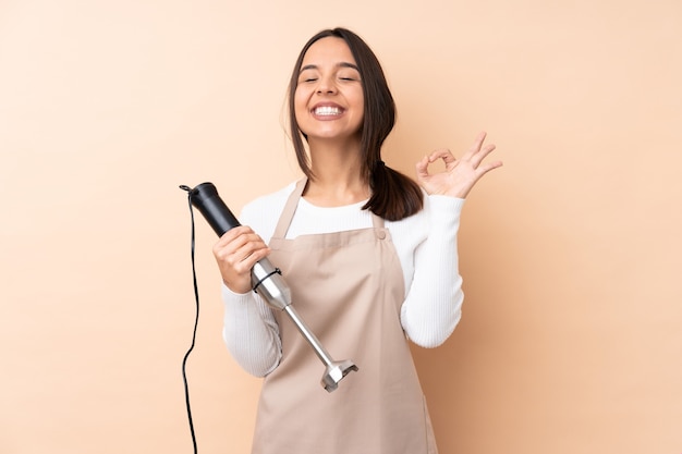 Jong donkerbruin meisje dat geïsoleerde handmixer met behulp van