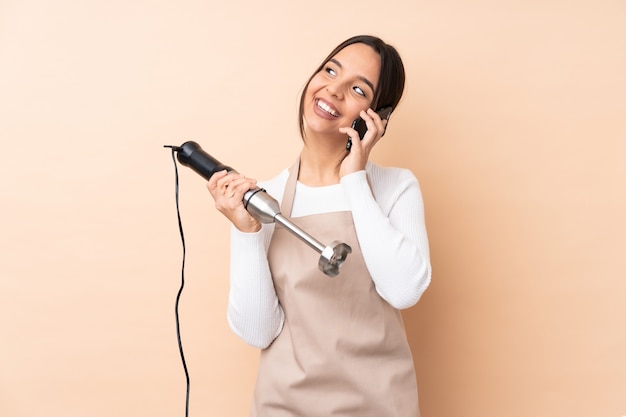 Jong donkerbruin meisje die de koffie van de handmixer om weg te halen en mobiel gebruiken