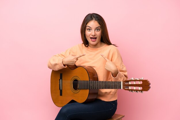 Jong donkerbruin meisje met gitaar over geïsoleerd roze met verrassingsgelaatsuitdrukking