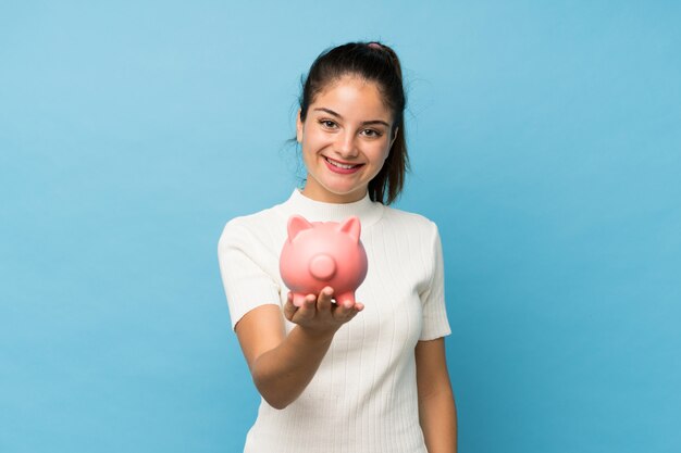 Jong donkerbruin meisje over geïsoleerd blauw dat een grote piggybank houdt