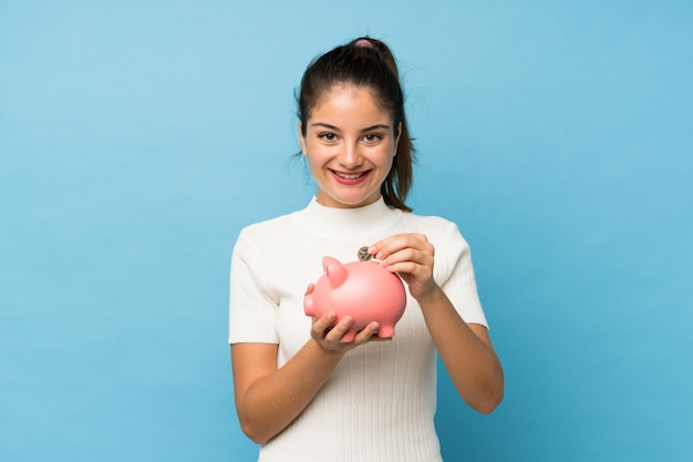 Jong donkerbruin meisje over geïsoleerd blauw dat een grote piggybank houdt