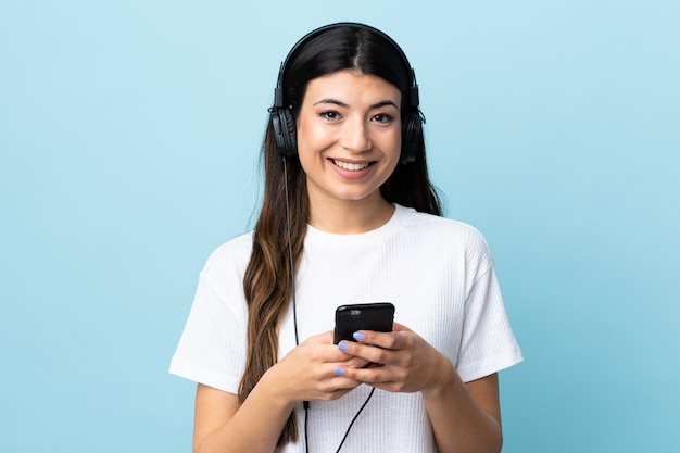 Jong donkerbruin meisje over geïsoleerde blauwe het luisteren muziek met mobiel en kijkend voorzijde