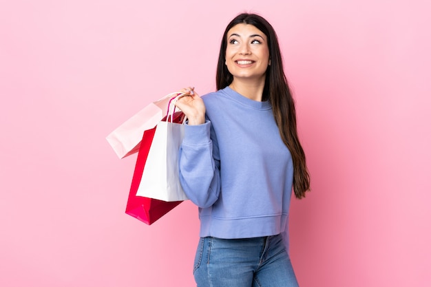 Jong donkerbruin meisje over geïsoleerde roze holding het winkelen zakken en het glimlachen