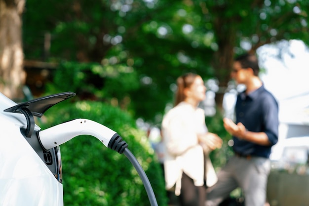 Jong echtpaar laadt de batterij van de elektrische auto op van een laadstation in een groen stadspark in de lente Oplaadbare elektrische auto voor een duurzame milieuvriendelijke stedelijke levensstijl