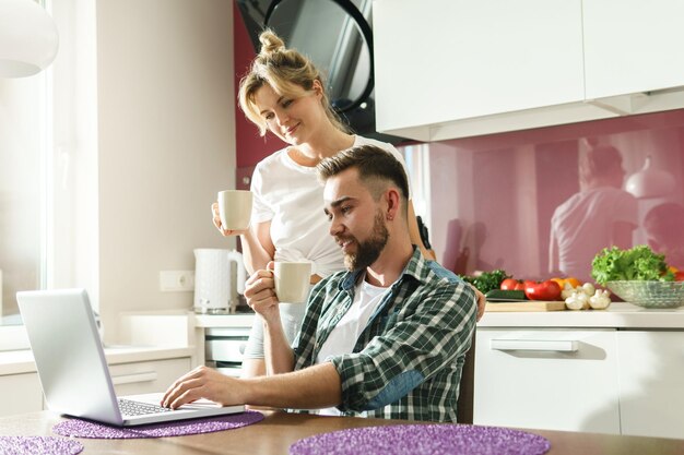 Jong en gelukkig paar dat 's ochtends laptop in de keuken gebruikt