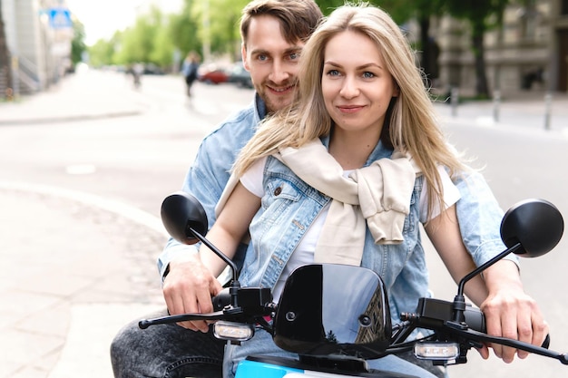 Jong en stijlvol stel dat plezier heeft tijdens het rijden op een elektrische scooter op straat in de stad