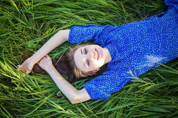 Jong Europees meisje in een blauwe jurk ligt in het gras met een hoed