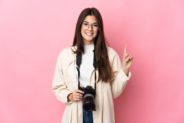 Jong fotograaf Braziliaans meisje dat op roze muur wordt geïsoleerd die en een vinger opheft als teken van het beste