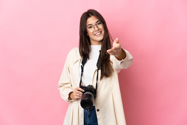 Jong fotograaf Braziliaans meisje geïsoleerd op roze muur handen schudden voor het sluiten van een goede deal