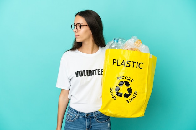 Jong Frans meisje dat een zak vol plastic flessen houdt om te recyclen op zoek naar de zijkant
