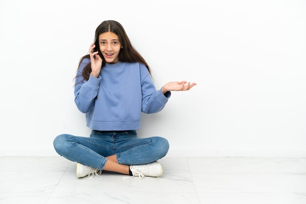 Jong Frans meisje dat op de grond zit en een gesprek voert met de mobiele telefoon met iemand