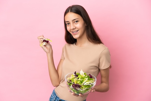 Jong Frans meisje dat op roze achtergrond wordt geïsoleerd die een kom salade met gelukkige uitdrukking houdt