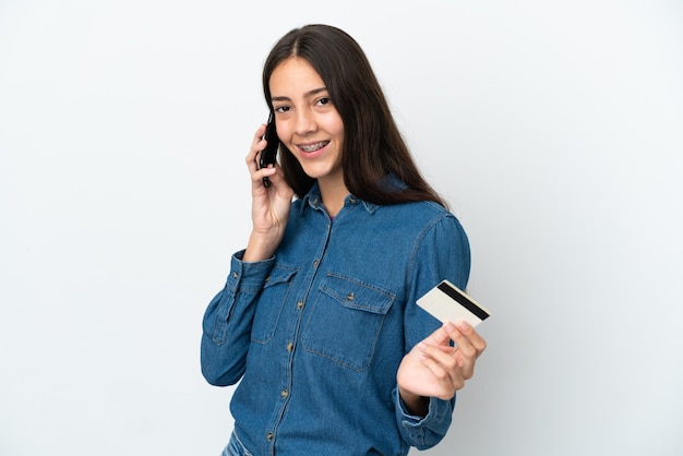 Jong Frans meisje dat op witte achtergrond wordt geïsoleerd die een gesprek met de mobiele telefoon houdt en een creditcard houdt