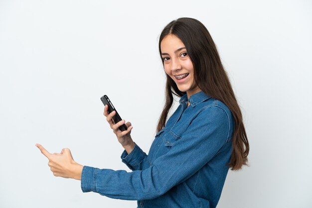 Jong Frans meisje geïsoleerd op een witte achtergrond met behulp van mobiele telefoon en terug te wijzen