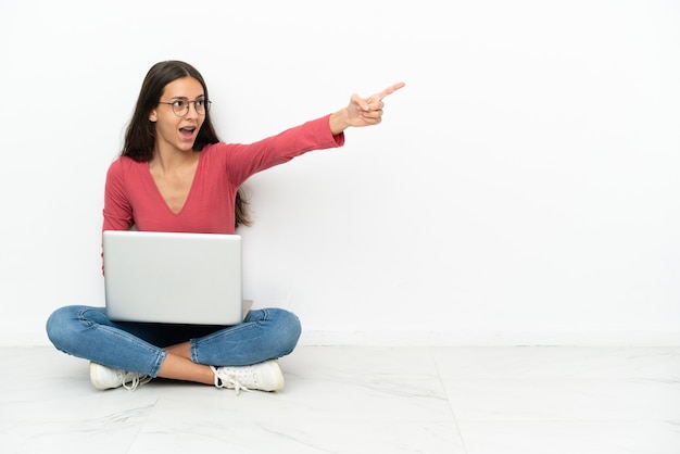 Jong Frans meisje zittend op de vloer met haar laptop wegwijzend