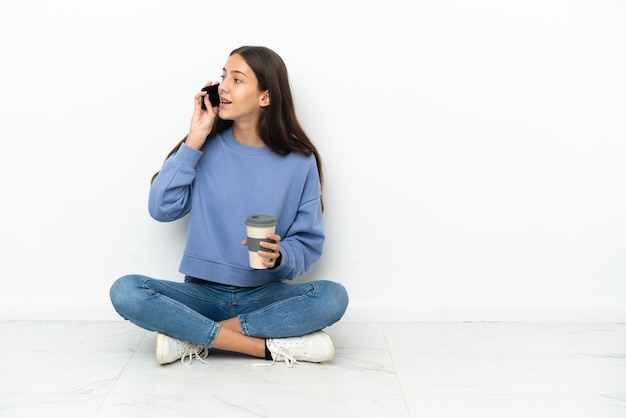 Jong Frans meisje zittend op de vloer met koffie om mee te nemen en een mobiel