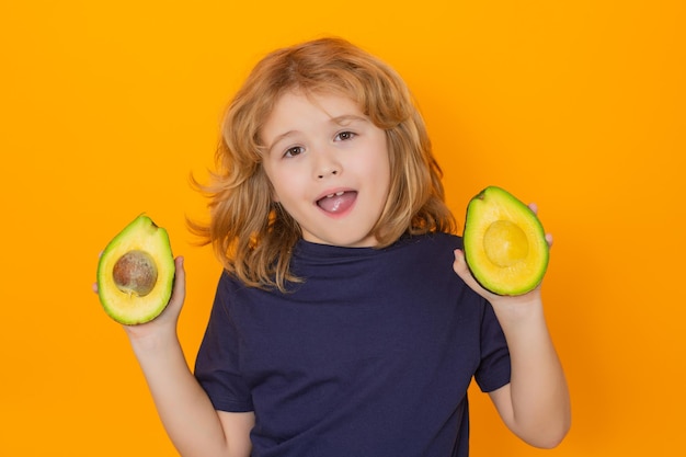 Jong geitje houdt rode avocado in studio Studioportret van leuk kind met avocado dat op gele achtergrondexemplaarruimte wordt geïsoleerd