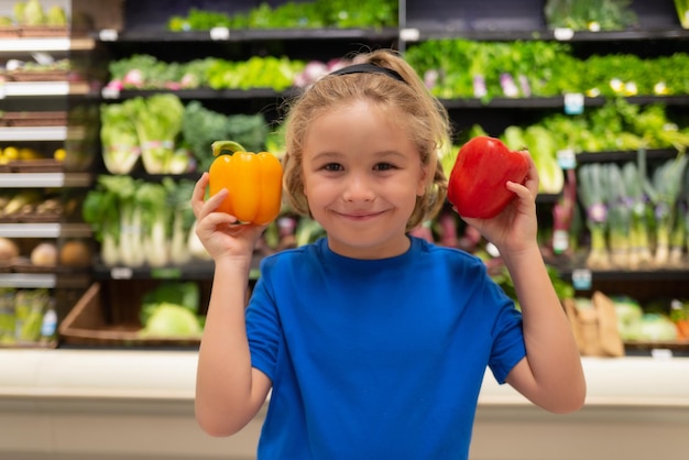 Jong geitje met groenten en pepers bij kruidenierswinkelopslag portret van kind in een voedselopslag of een supermarkt