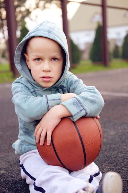 Jong geitjezitting met basketbalbal op het gebied van de basketbalstraat