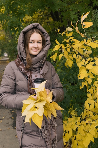 Jong geluk mooi meisje met met koffie en gele bladeren Kleuren van de herfst herfst seizoen