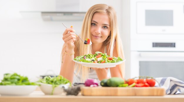 Jong gelukkig blond meisje dat gezonde salade eet van rucola, spinazie, tomaten, olijven, ui en olijfolie.