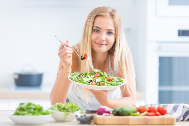 Jong gelukkig blond meisje dat gezonde salade eet van rucola, spinazie, tomaten, olijven, ui en olijfolie.