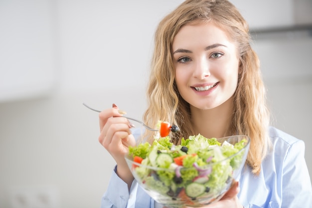 Jong gelukkig blondemeisje die gezonde salade eten.