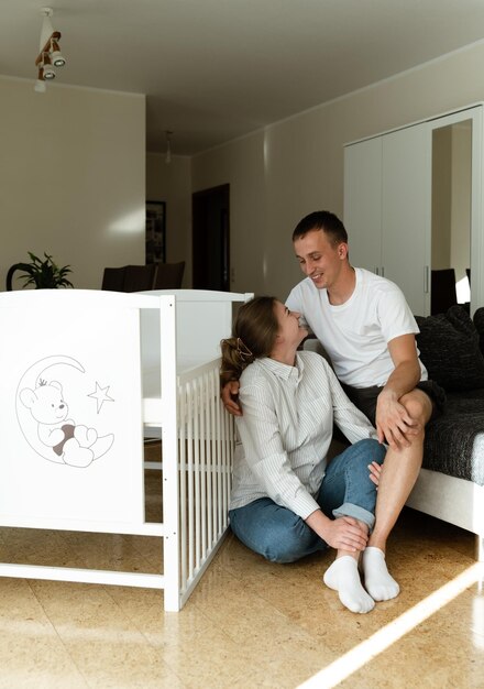 Foto jong gelukkig echtpaar in hun nieuwe huis een zwangere vrouw en haar man zitten bij de wieg
