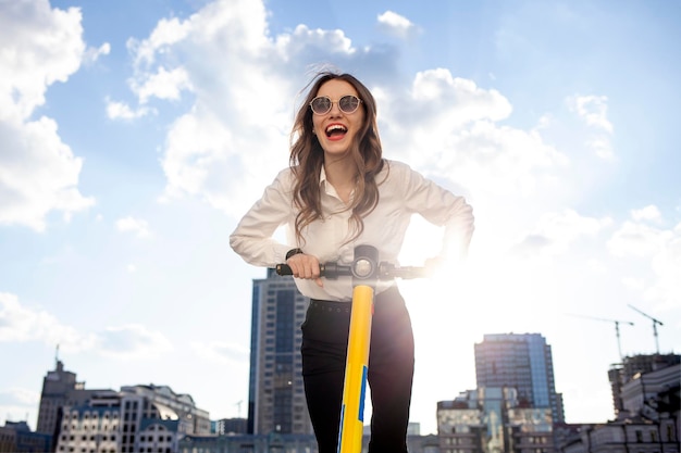 jong gelukkig meisje in zonnebril rijdt vooruit op elektrische scooter en schreeuwt op straat