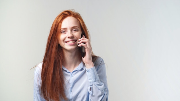 Jong gelukkig mooi roodharig meisje dat op de telefoon spreekt die bij de camera glimlacht