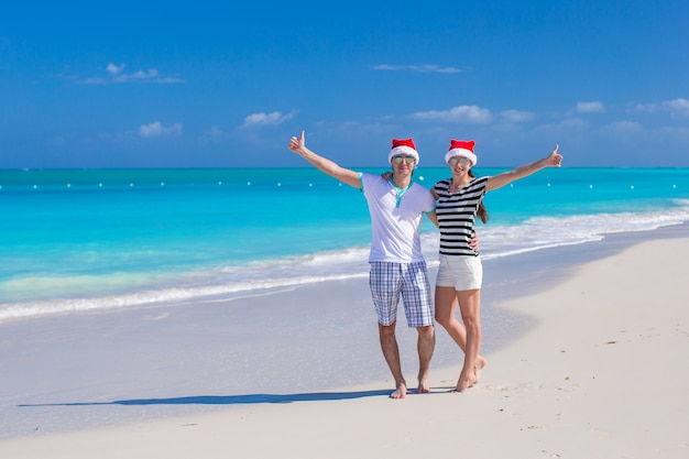 Jong gelukkig paar in rode Kerstmanhoeden op tropisch strand