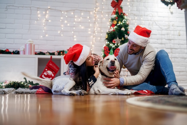 Jong gelukkig paar knuffelen schattige witte hond met tong uit voor kerstvakantie thuis.