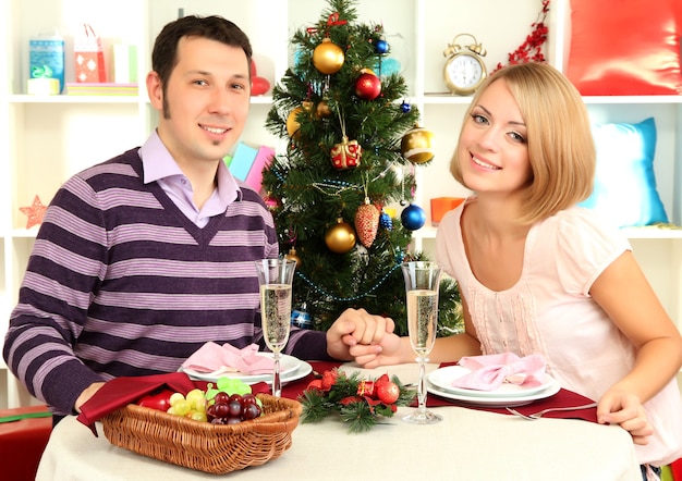 Jong gelukkig paar met champagne aan tafel in de buurt van de kerstboom