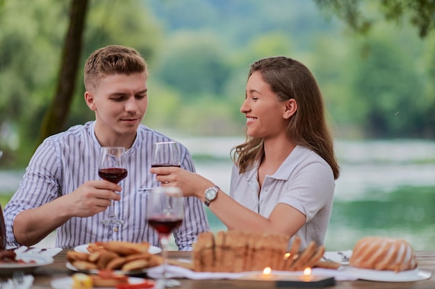 jong gelukkig stel dat rode wijnglas roostert terwijl ze picknick Frans etentje buiten hebben tijdens de zomervakantie vakantie in de buurt van de rivier in de prachtige natuur