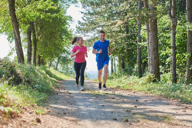 jong gelukkig stel geniet van een gezonde levensstijl tijdens het joggen op een landweg door het prachtige zonnige bos, lichaamsbeweging en fitnessconcept