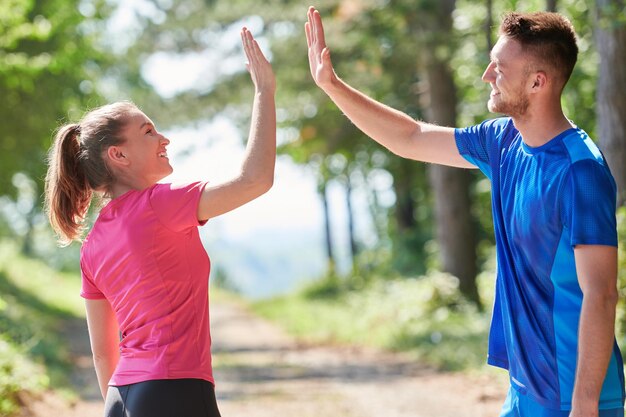 jong gelukkig stel geniet van een gezonde levensstijl tijdens het joggen op een landweg door het prachtige zonnige bos, lichaamsbeweging en fitnessconcept