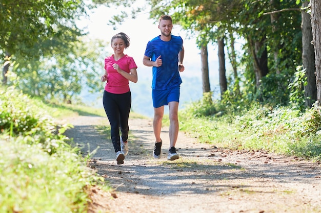 jong gelukkig stel geniet van een gezonde levensstijl tijdens het joggen op een landweg door het prachtige zonnige bos, lichaamsbeweging en fitnessconcept