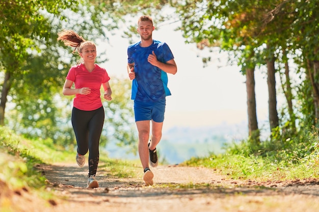 jong gelukkig stel geniet van een gezonde levensstijl tijdens het joggen op een landweg door het prachtige zonnige bos, lichaamsbeweging en fitnessconcept