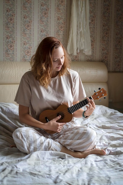 Jong gelukkig vrolijk meisje dat het ukeleleportret leert van een meisje dat thuis ukelele speelt