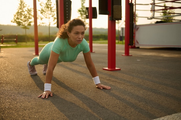 Jong gemengd ras, Afro-Amerikaanse vrouw atleet die buiten traint, push-ups doet op sportveld in de zomer. Gezonde actieve levensstijl en fitness concept