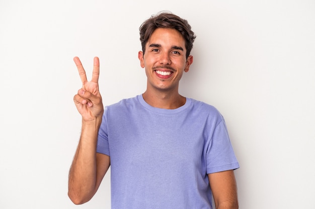 Jong gemengd ras man geïsoleerd op een witte achtergrond blij en zorgeloos met een vredessymbool met vingers.