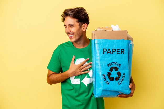 Jong gemengd ras man recycling papier geïsoleerd op gele achtergrond lachen en plezier hebben.