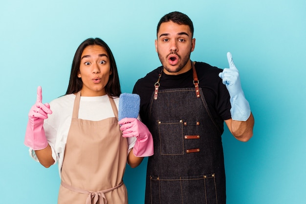 Jong gemengd ras paar schoonmaak huis geïsoleerd op blauwe achtergrond met een geweldig idee, concept van creativiteit.