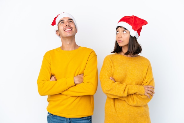 Jong gemengd ras paar vieren Kerstmis geïsoleerd op een witte achtergrond opzoeken terwijl u lacht