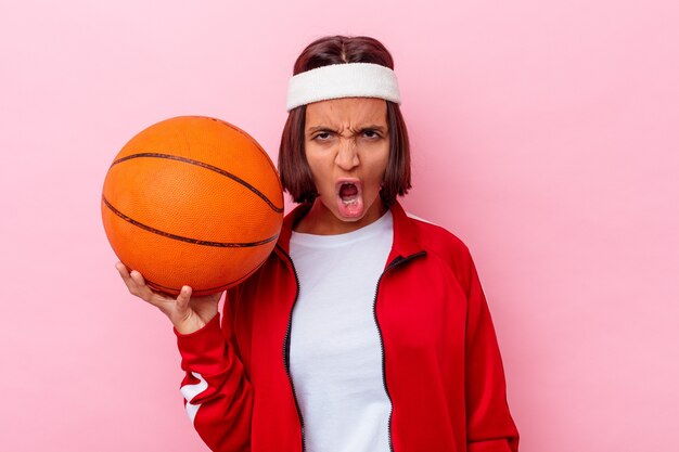 Jong gemengd ras vrouw speelbasketbal geïsoleerd op roze achtergrond schreeuwen erg boos en agressief.