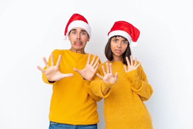 Jong gemengd raspaar dat Kerstmis viert dat op een witte achtergrond wordt geïsoleerd, is een beetje nerveus en bang om de handen naar voren te strekken