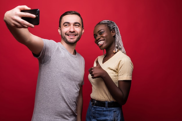 Jong gemengd raspaar, Kaukasische man en Afrikaanse vrouw die selfie van telefoon nemen terwijl status op rode achtergrond