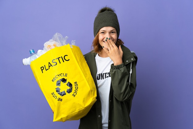 Jong Georgisch meisje dat een zak vol plastic flessen houdt om gelukkig en glimlachend te recyclen die mond met hand bedekken