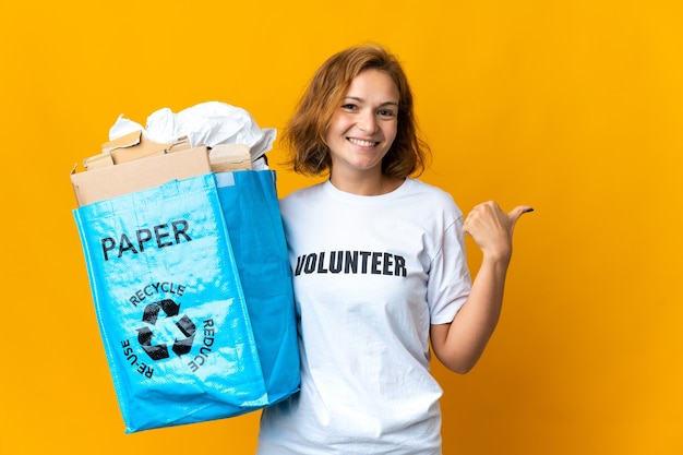 Jong Georgisch meisje met een recyclezak vol papier om te recyclen, wijzend naar de zijkant om een product te presenteren